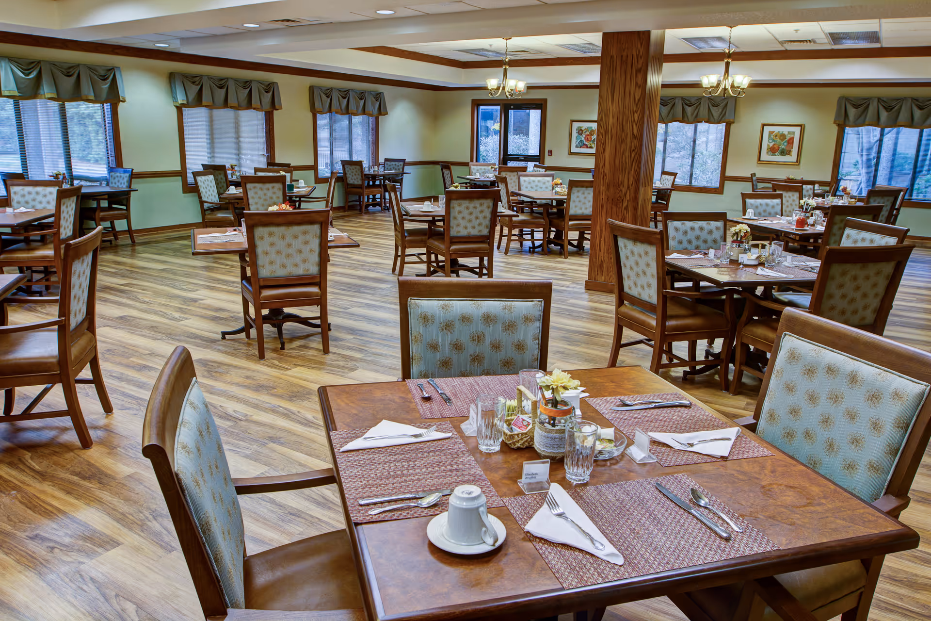 A spacious dining room with arranged tables and chairs, soft lighting, windows, and wooden floors visible.