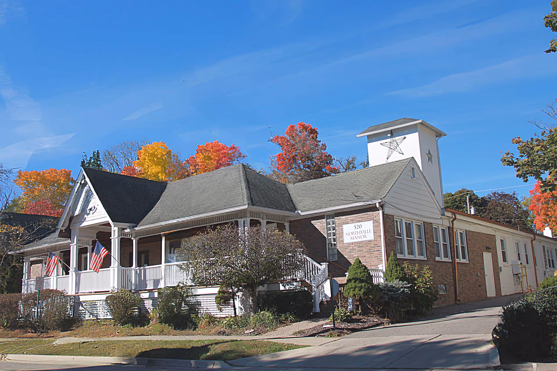 Exterior view of Star Manor of Northville with a brick building, porch, and autumn trees.