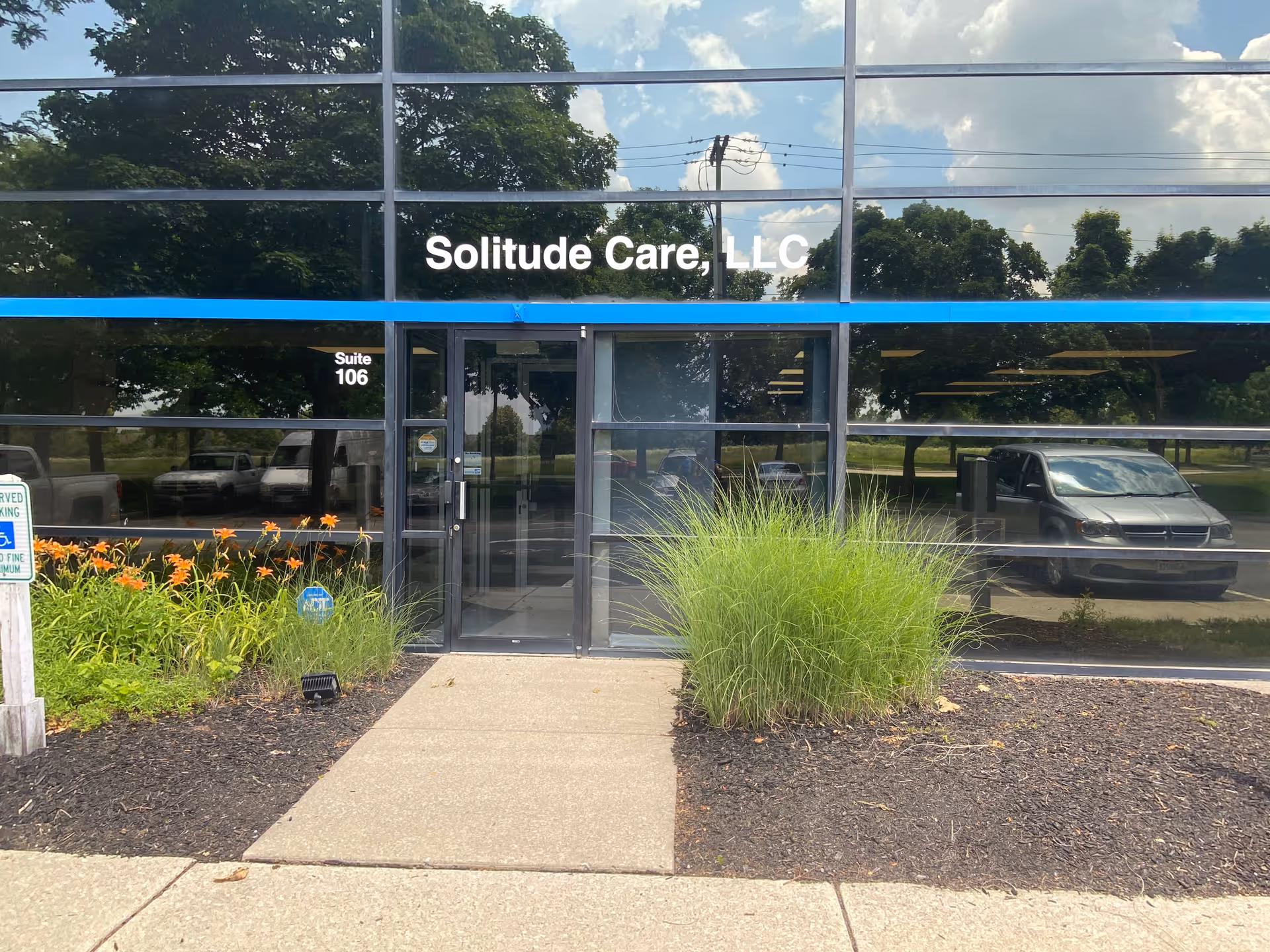 Front of Solitude Care LLC building with glass facade, entrance, and landscaped plants.