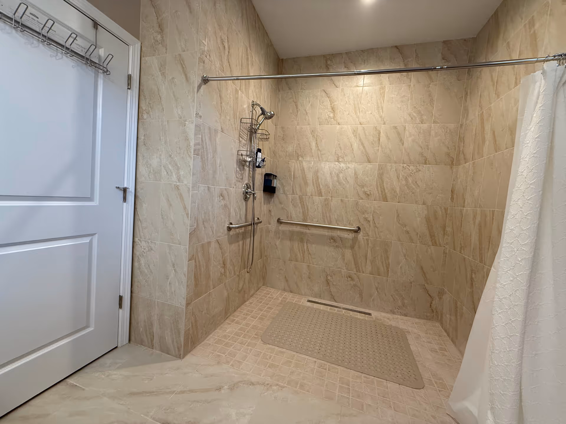 Walk-in tiled bathroom shower with grab bars, a shower head, and a textured floor mat.
