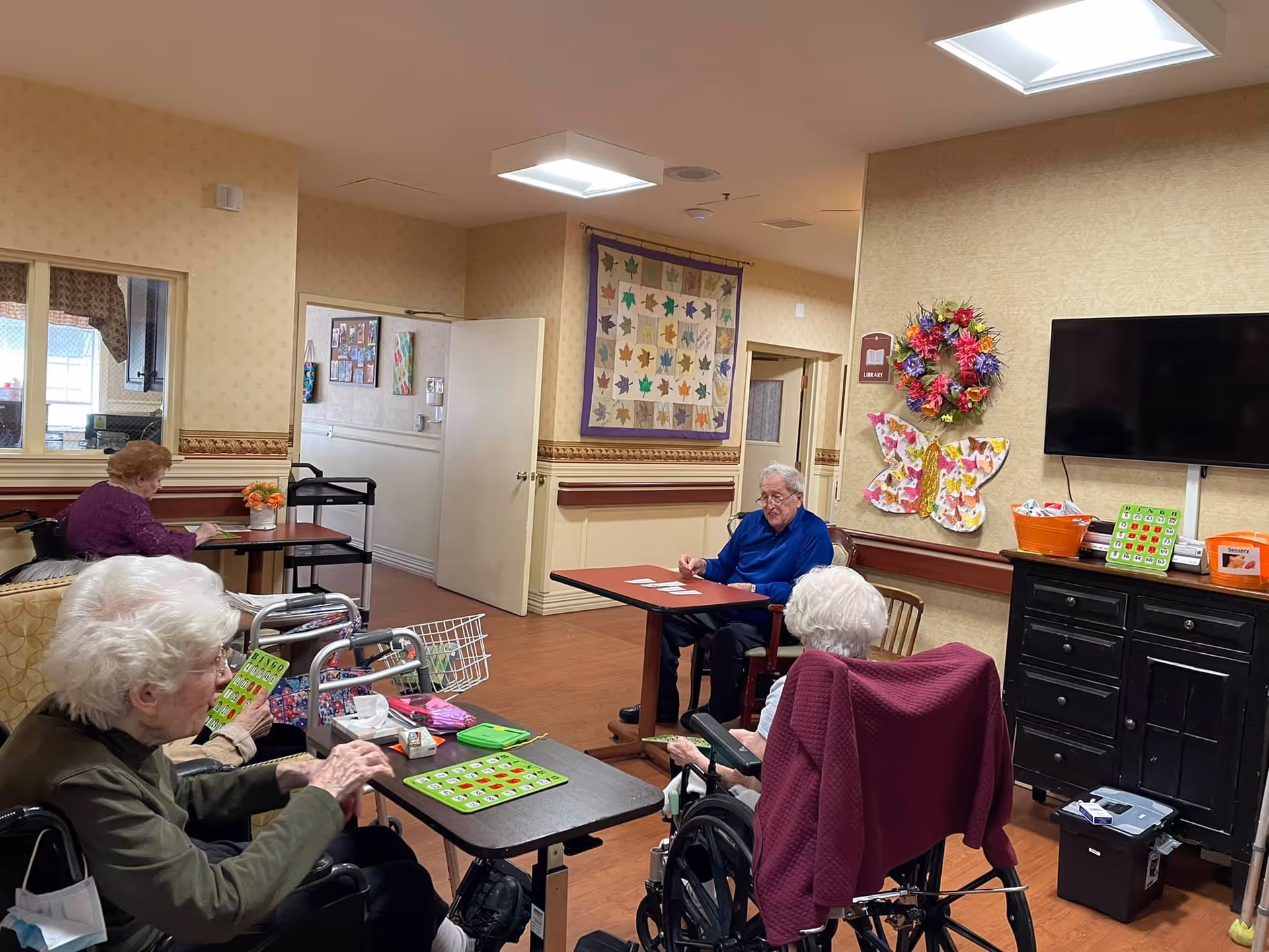 Elderly residents socialize at tables in a cozy Prescott House common room.