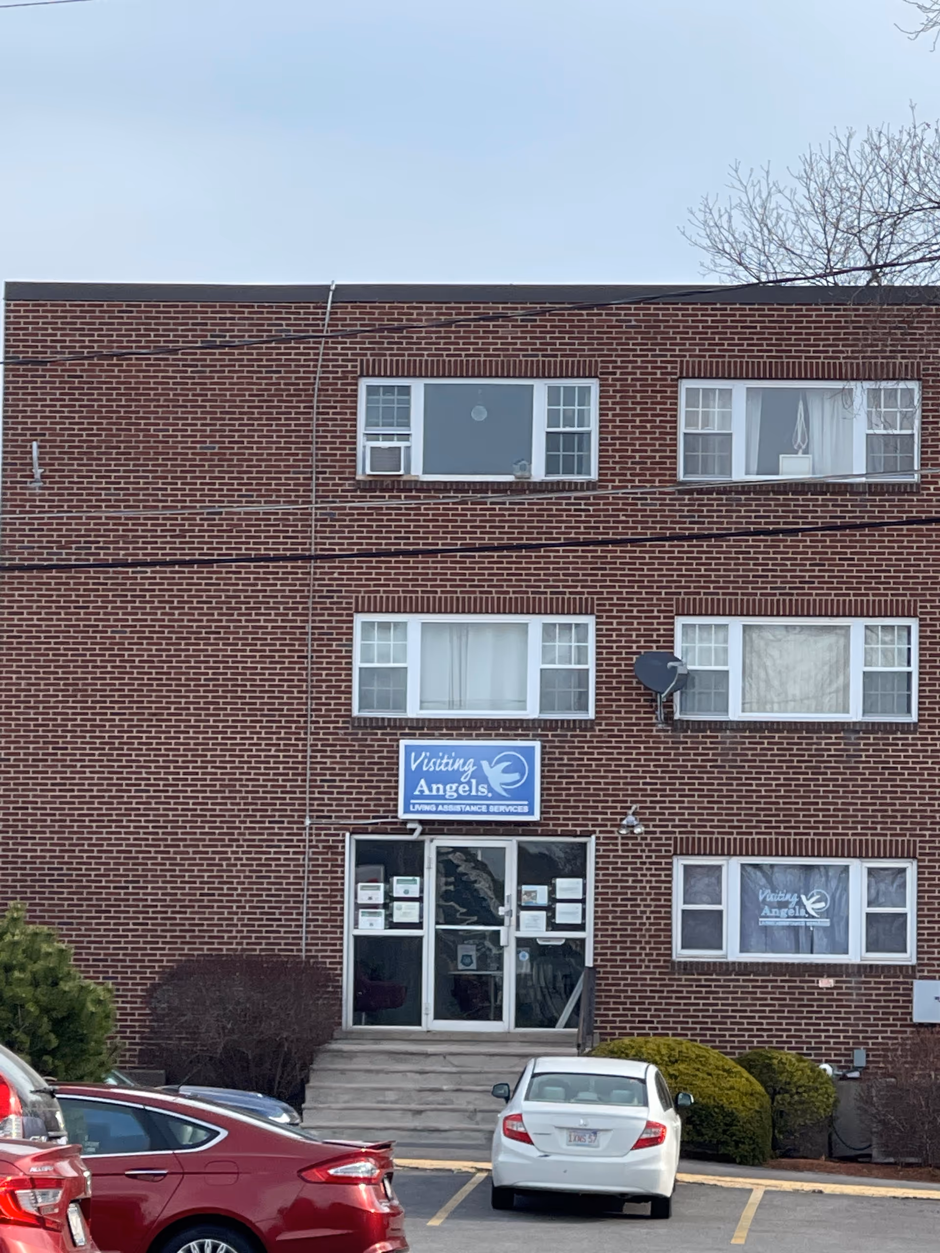 Brick senior home care building with entrance, parked cars, and Visiting Angels sign.