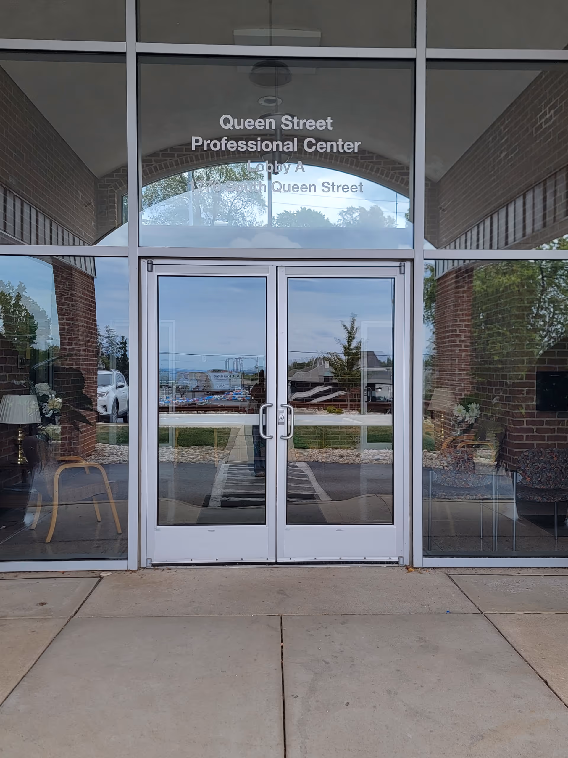 Glass doors of a brick building entrance with reflections and a Queen Street Professional Center sign