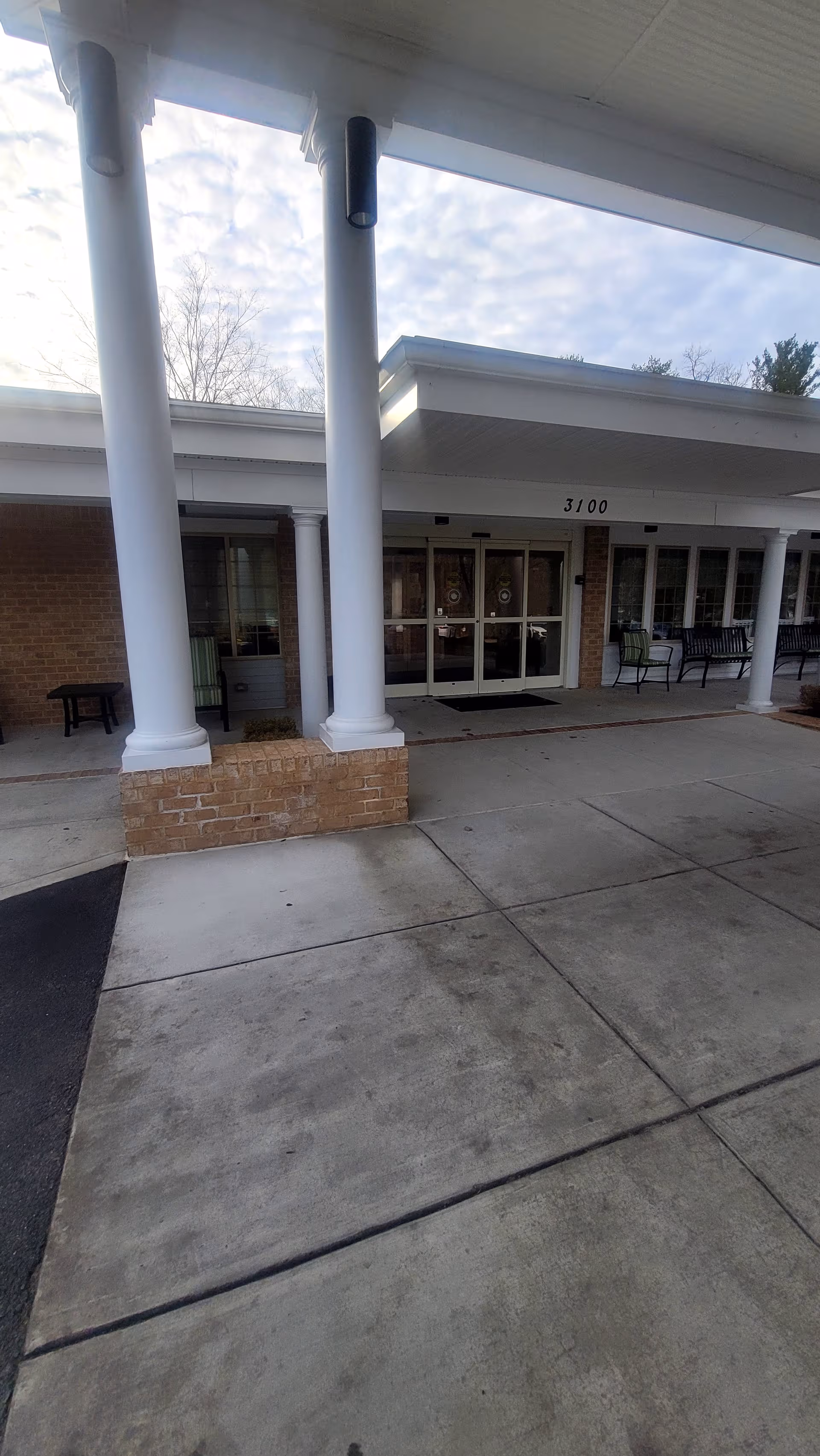 Exterior entrance of Lighthouse Senior Living at Ellicott City with white pillars and glass doors.