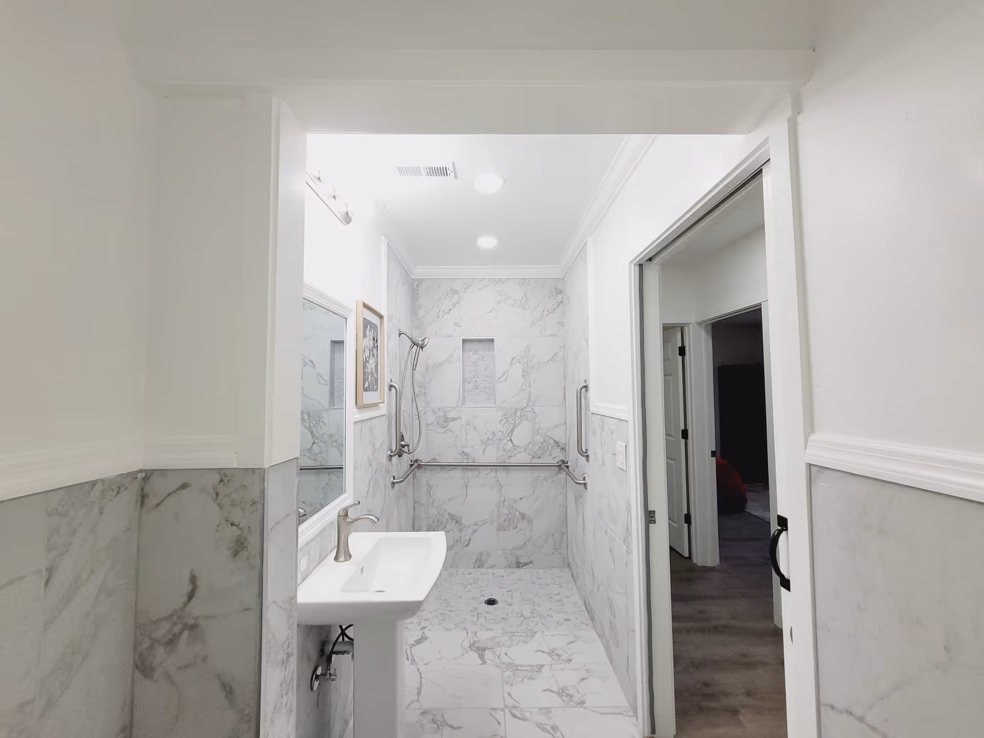 Bright marble-tiled bathroom with sink, shower, and safety grab bars.