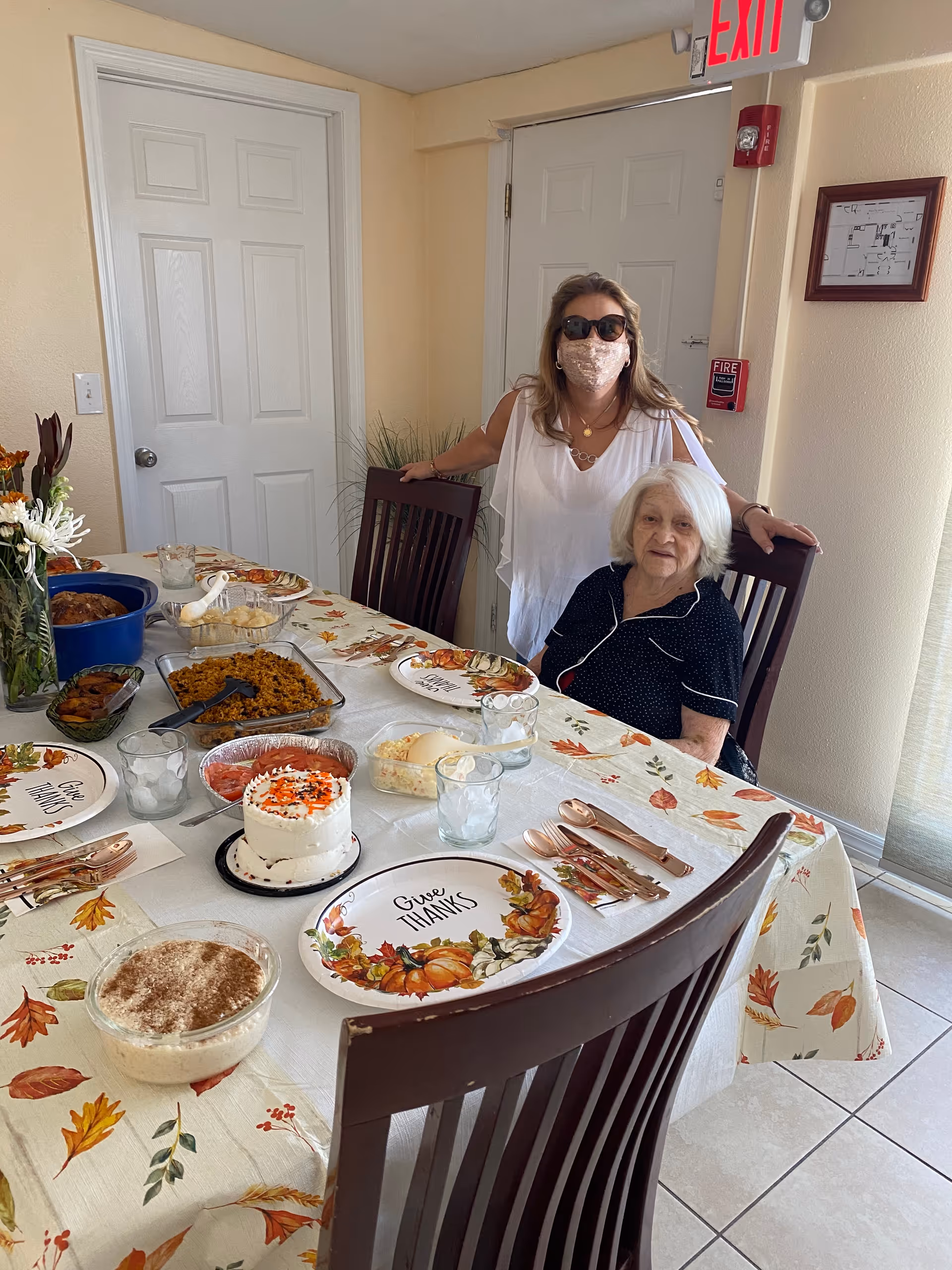 Two women pose at a dining table set with Thanksgiving-themed plates, desserts, and side dishes.