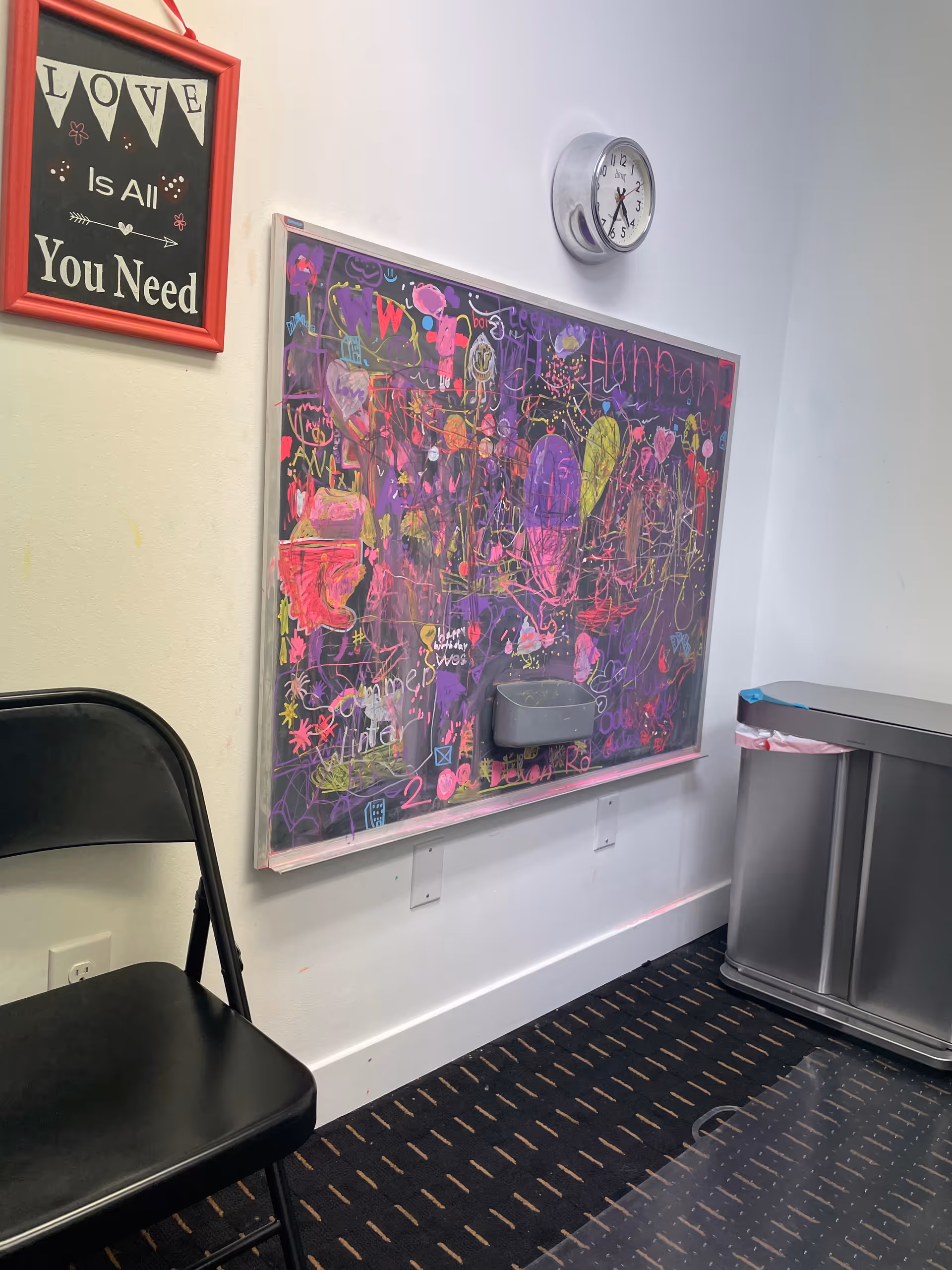 Colorful chalkboard art on a hallway wall beside a clock and chair.