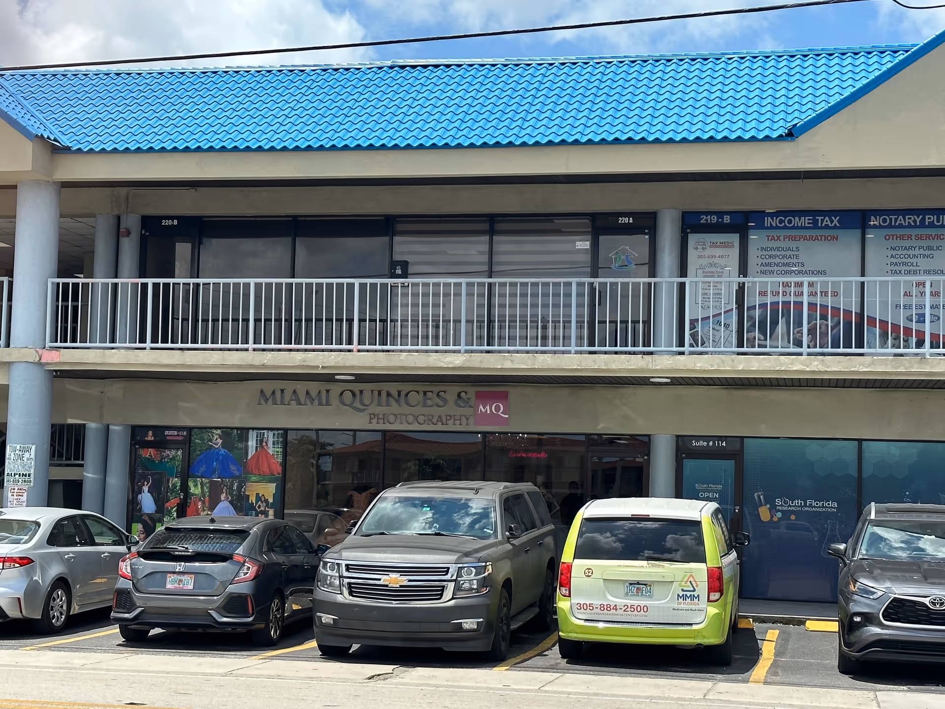 Two-story strip mall with storefronts, including a photography shop, and several parked cars.