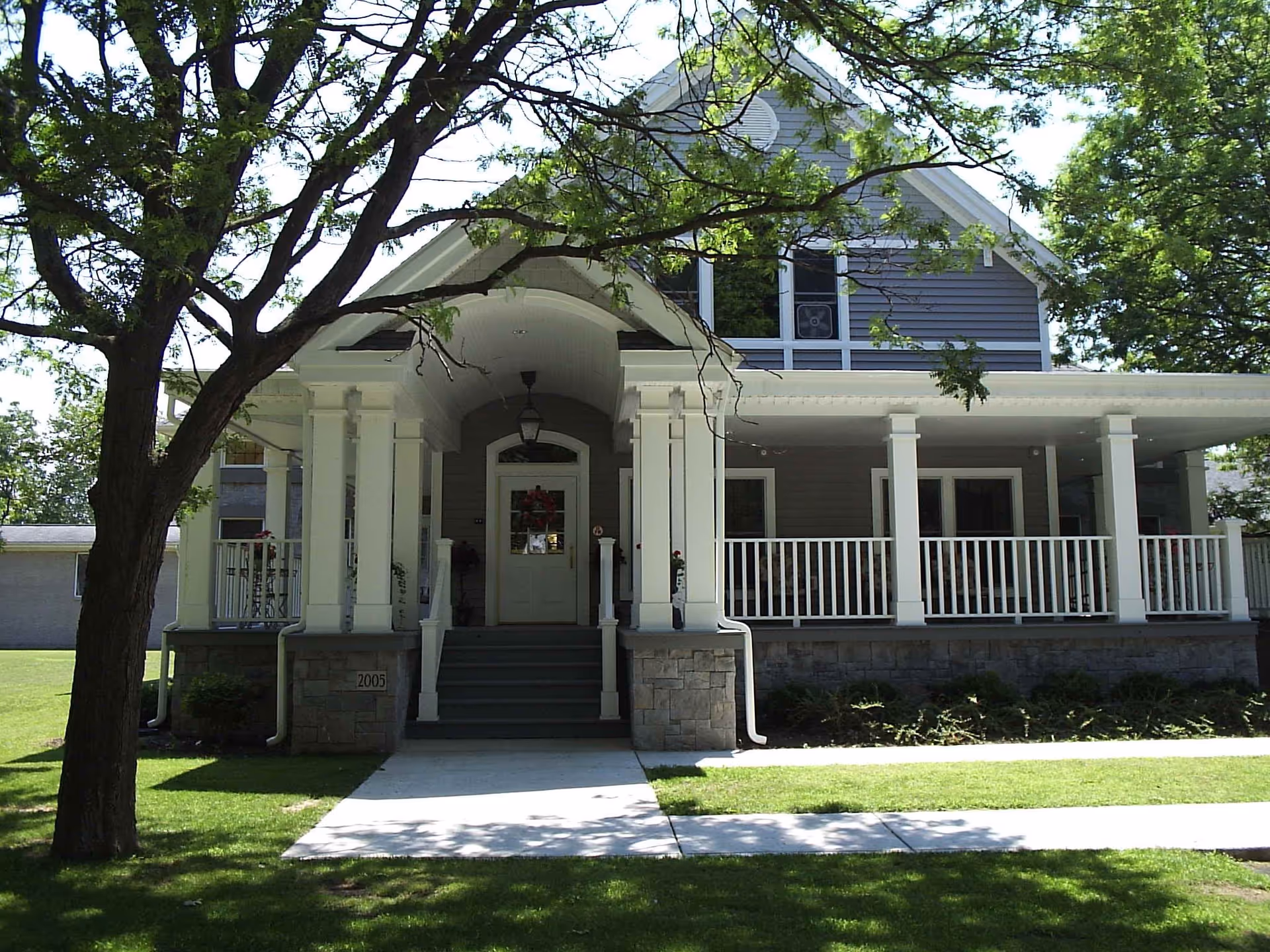Front exterior of a two-story house with a covered porch, white columns, and a tree-lined lawn.