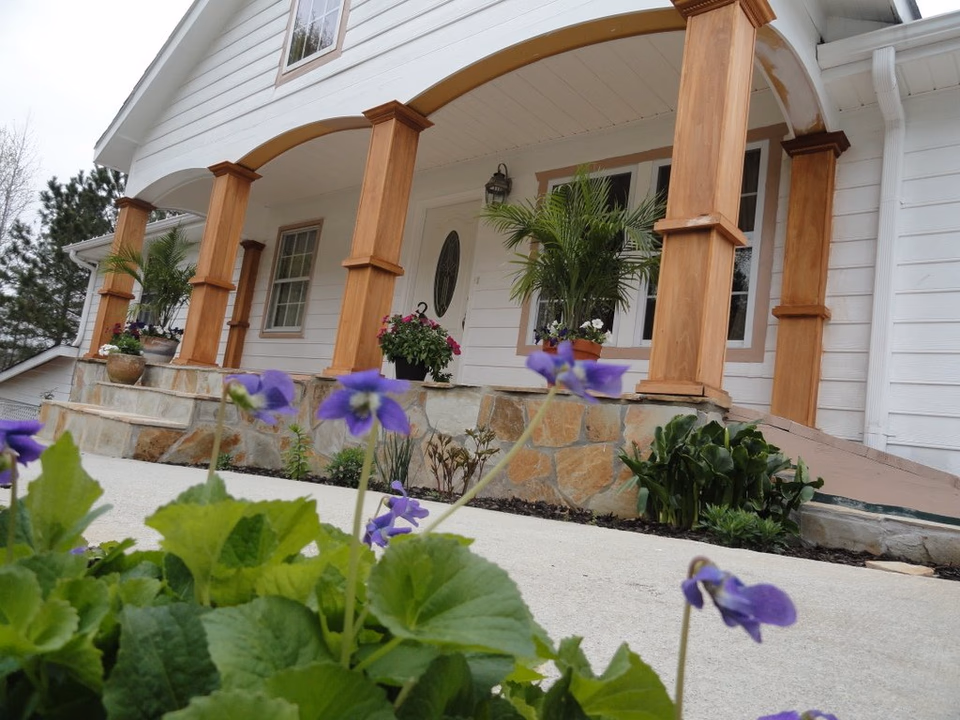 Front porch of a house with wooden columns, stone steps, and potted flowers.