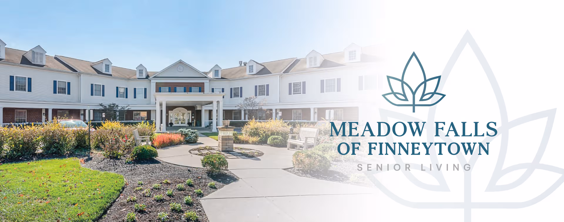 Exterior view of a white senior living facility with a landscaped entrance and benches.