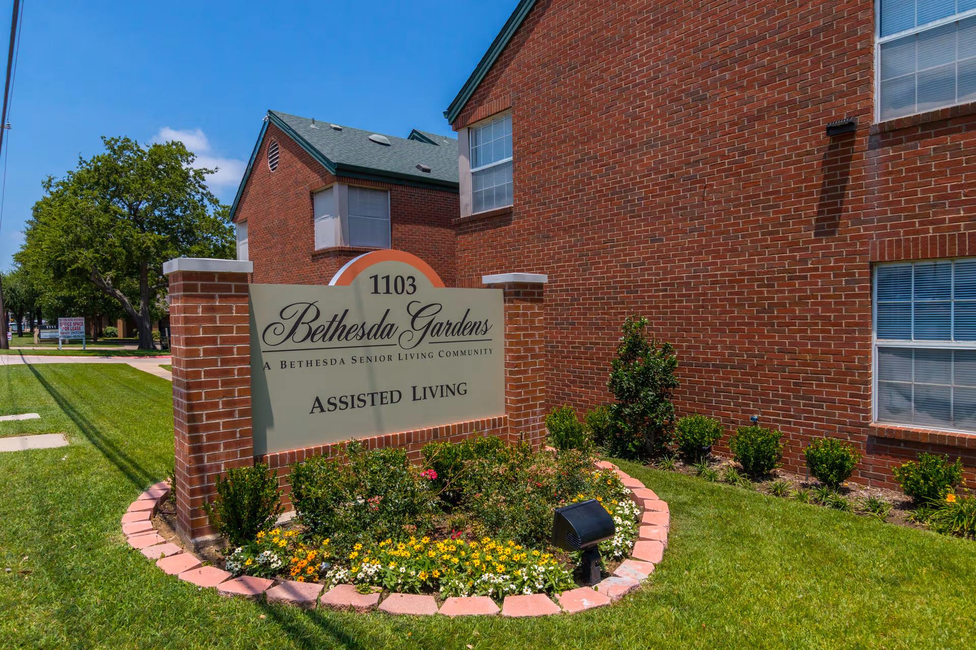 Brick Bethesda Gardens sign on a landscaped front lawn with an assisted living building.