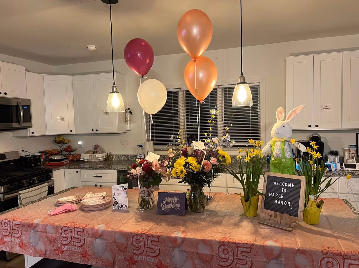 Bright kitchen with white cabinets, balloons, flowers, and a birthday party table.