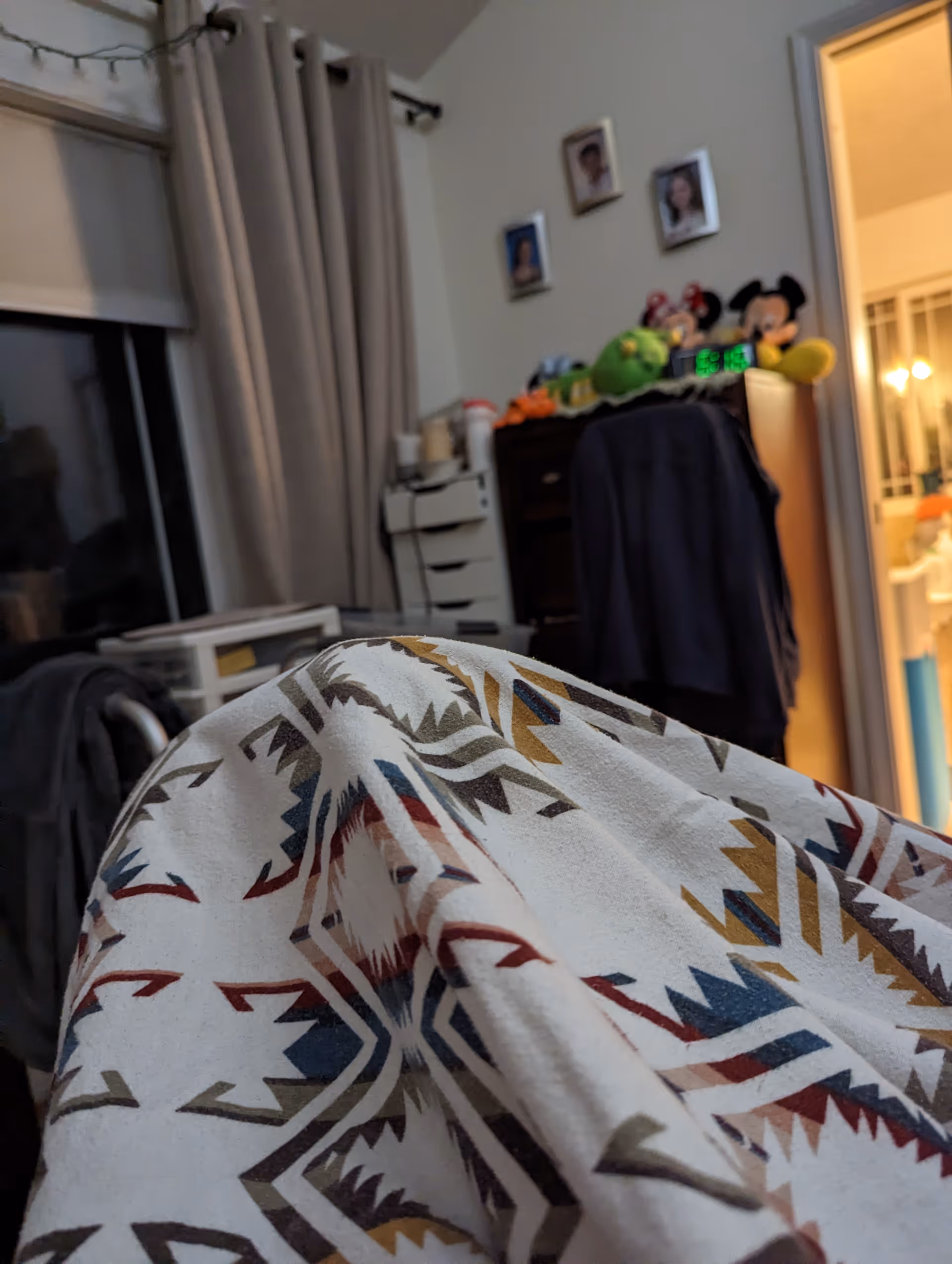 Bedroom interior with geometric blanket in the foreground, curtains, dresser, and framed photos.