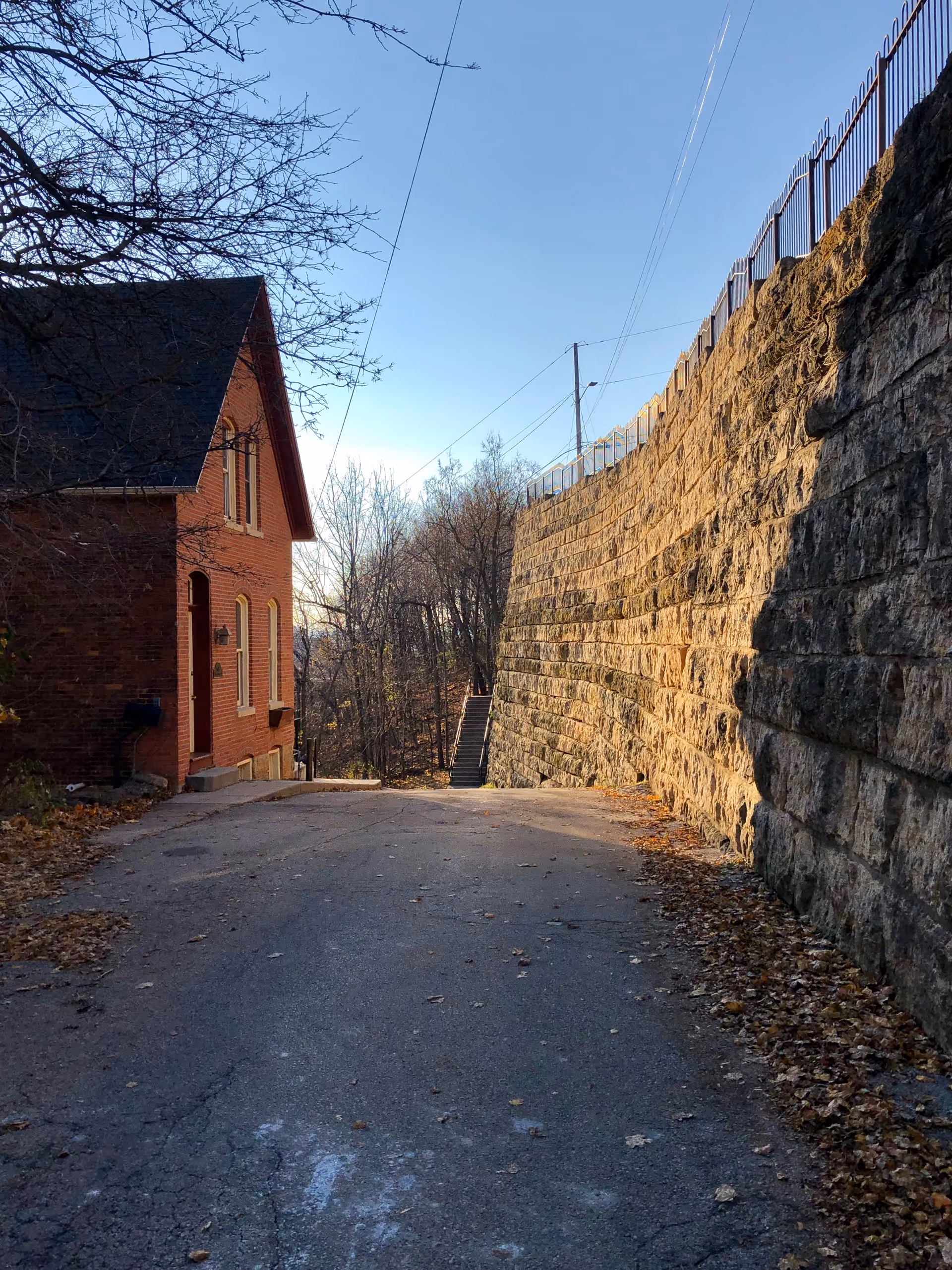 Narrow outdoor path beside a brick building and a tall stone wall with stairs.
