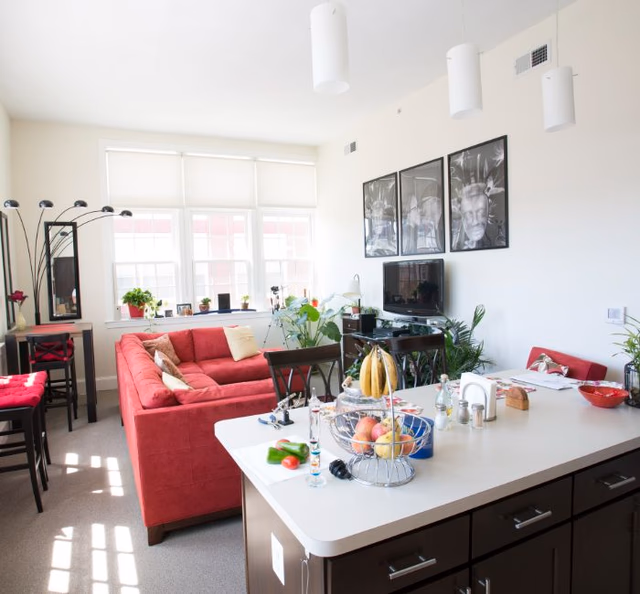 Bright open living area with red sofa, kitchen island, plants, and wall art.