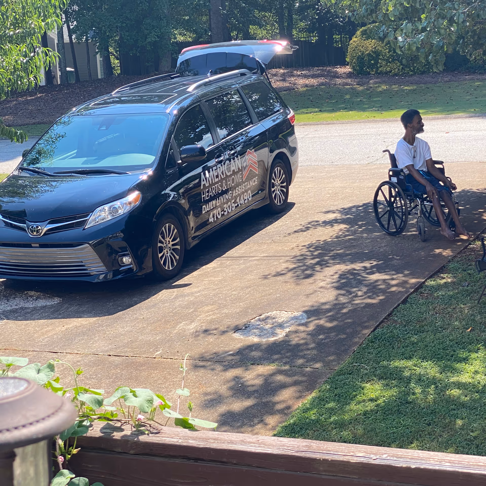 A branded American Hearts and Home van beside a resident in a wheelchair outdoors.