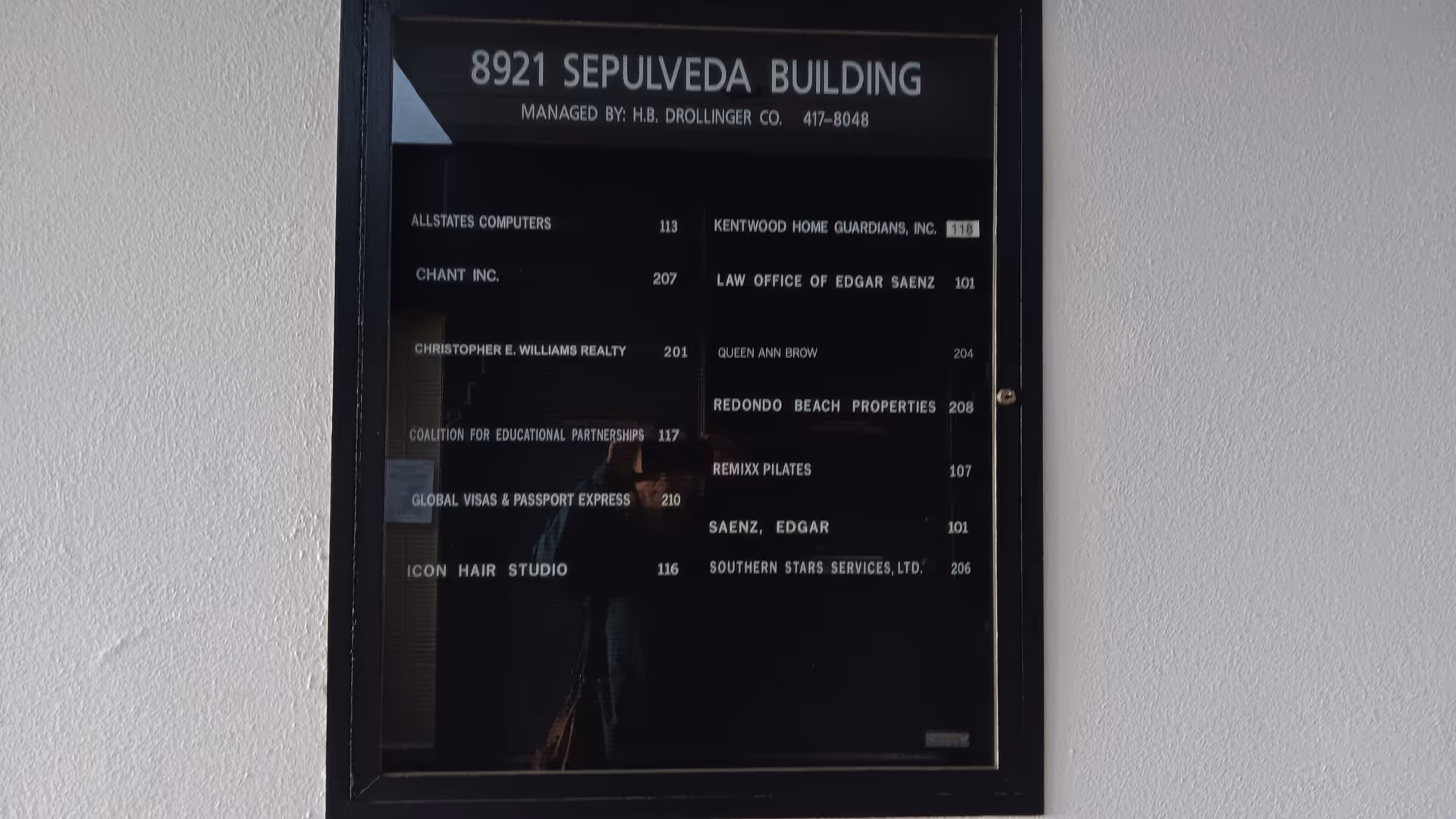 A framed building directory plaque listing tenants mounted on a pale wall.