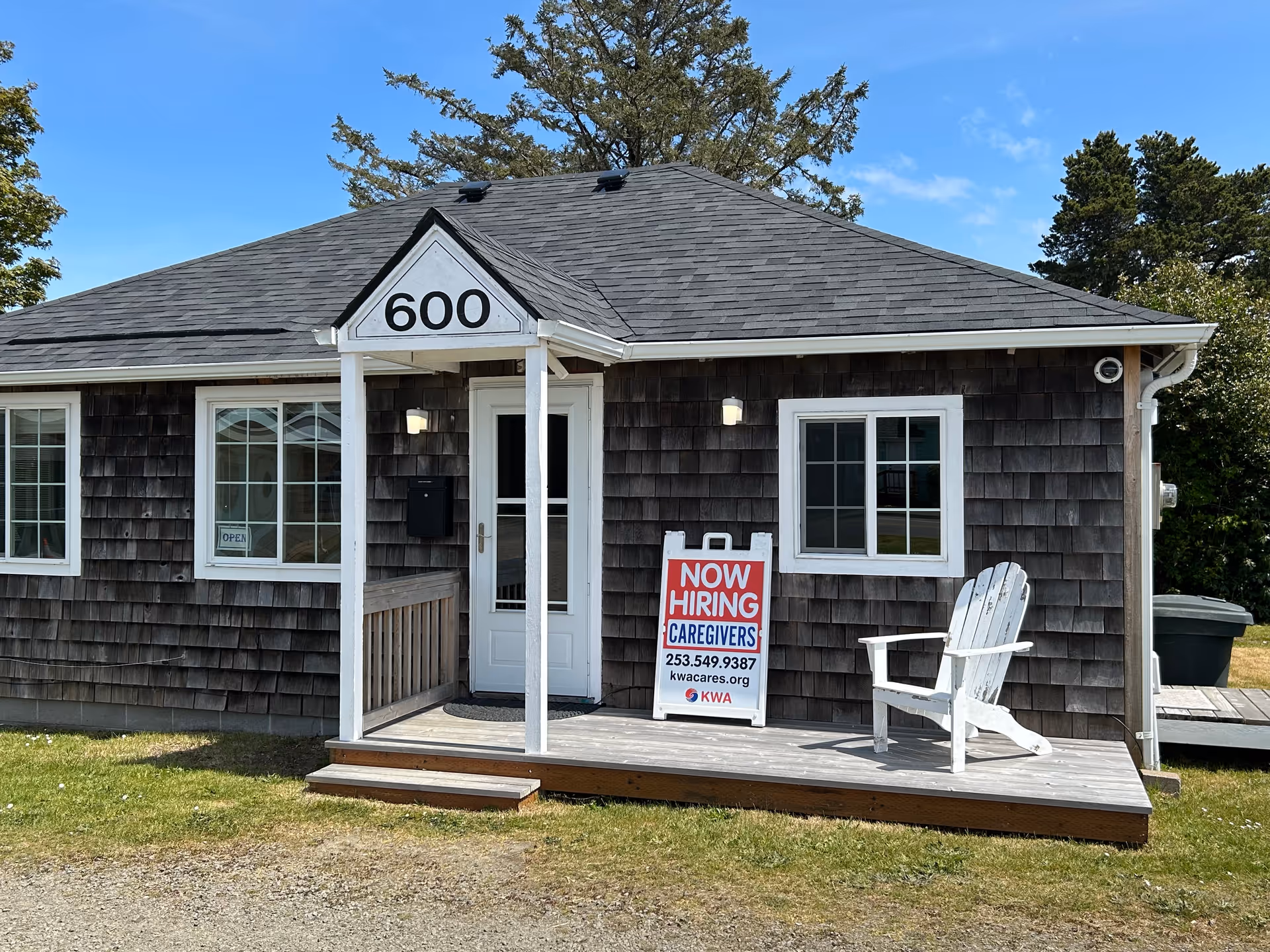 Small brown shingled building with a front porch and a Now Hiring Caregivers sign.