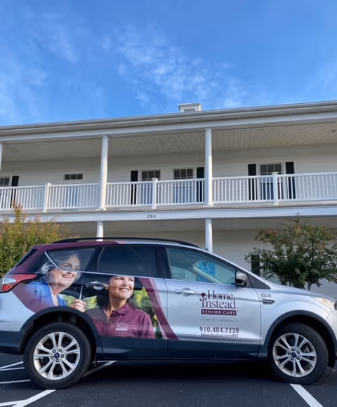 Two-story senior living facility exterior with a branded Home Instead vehicle parked out front.