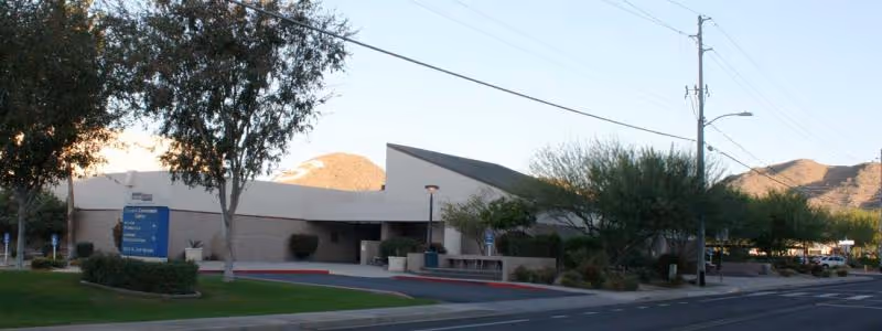 Exterior view of a single-story medical facility with landscaping and mountains in the background.