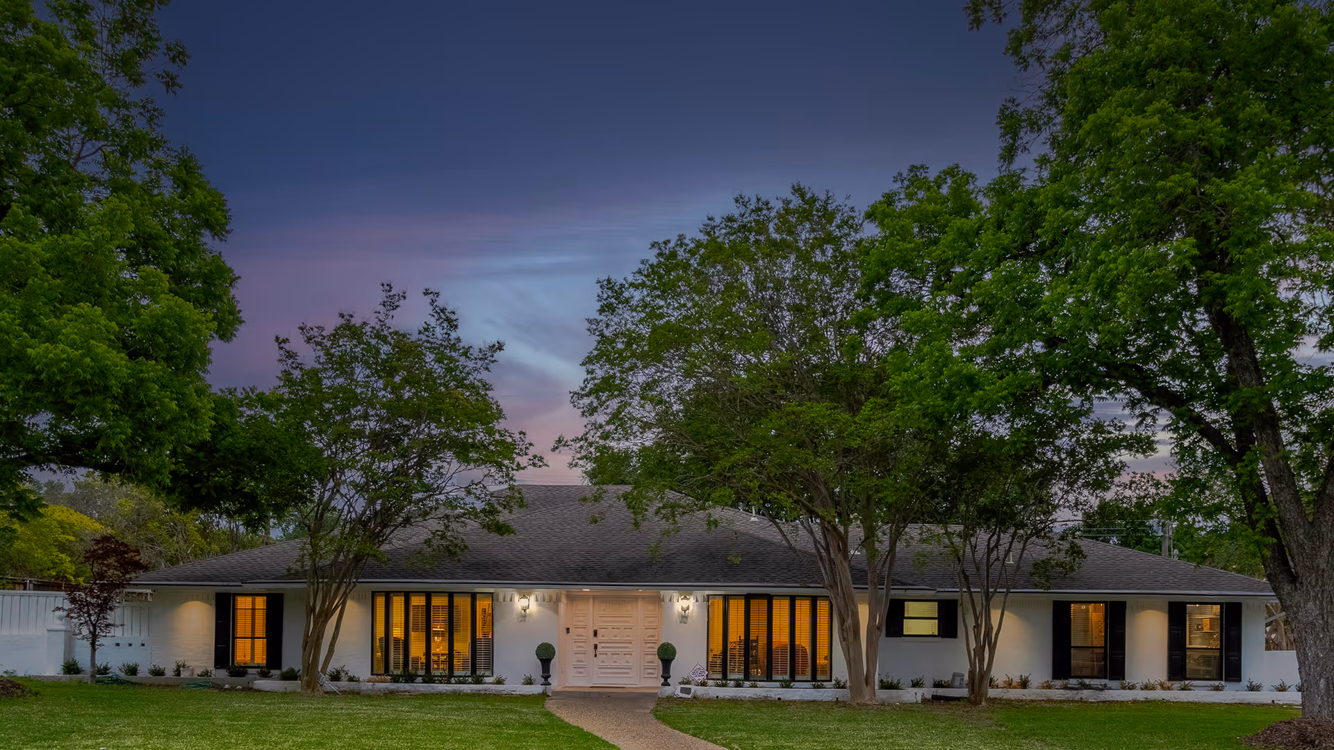 Single-story senior living facility exterior with large windows and trees at dusk.