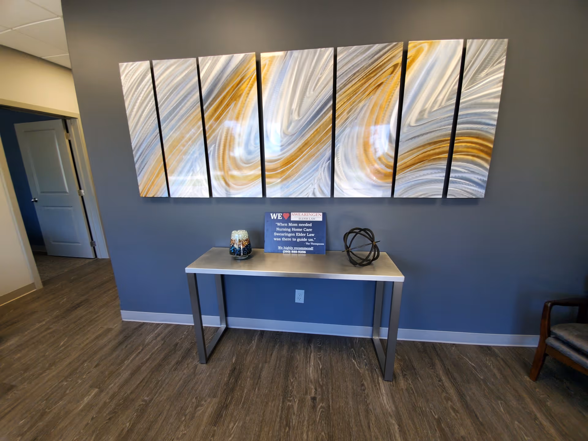 Blue-walled hallway with six-panel abstract art above a metal-framed console table.