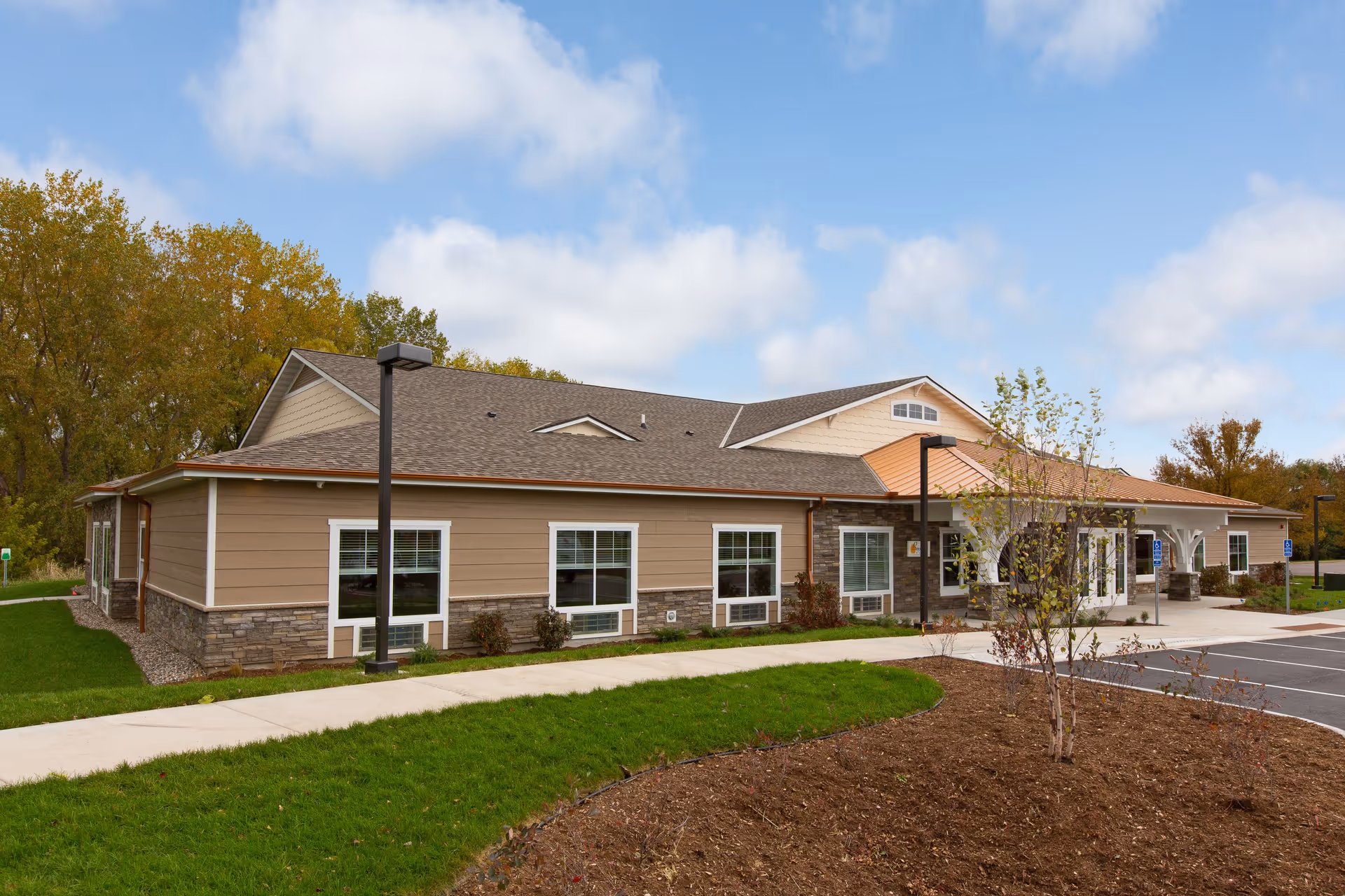 Single-story Beehive Homes exterior with beige siding, stone accents, and a sidewalk.
