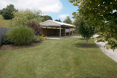 Lawn area with a covered outdoor pavilion beside Hillsville Health & Rehab Center, surrounded by trees.