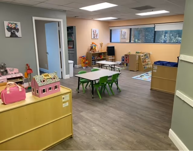 Colorful children's play area with small tables, chairs, and toy shelves inside a facility.