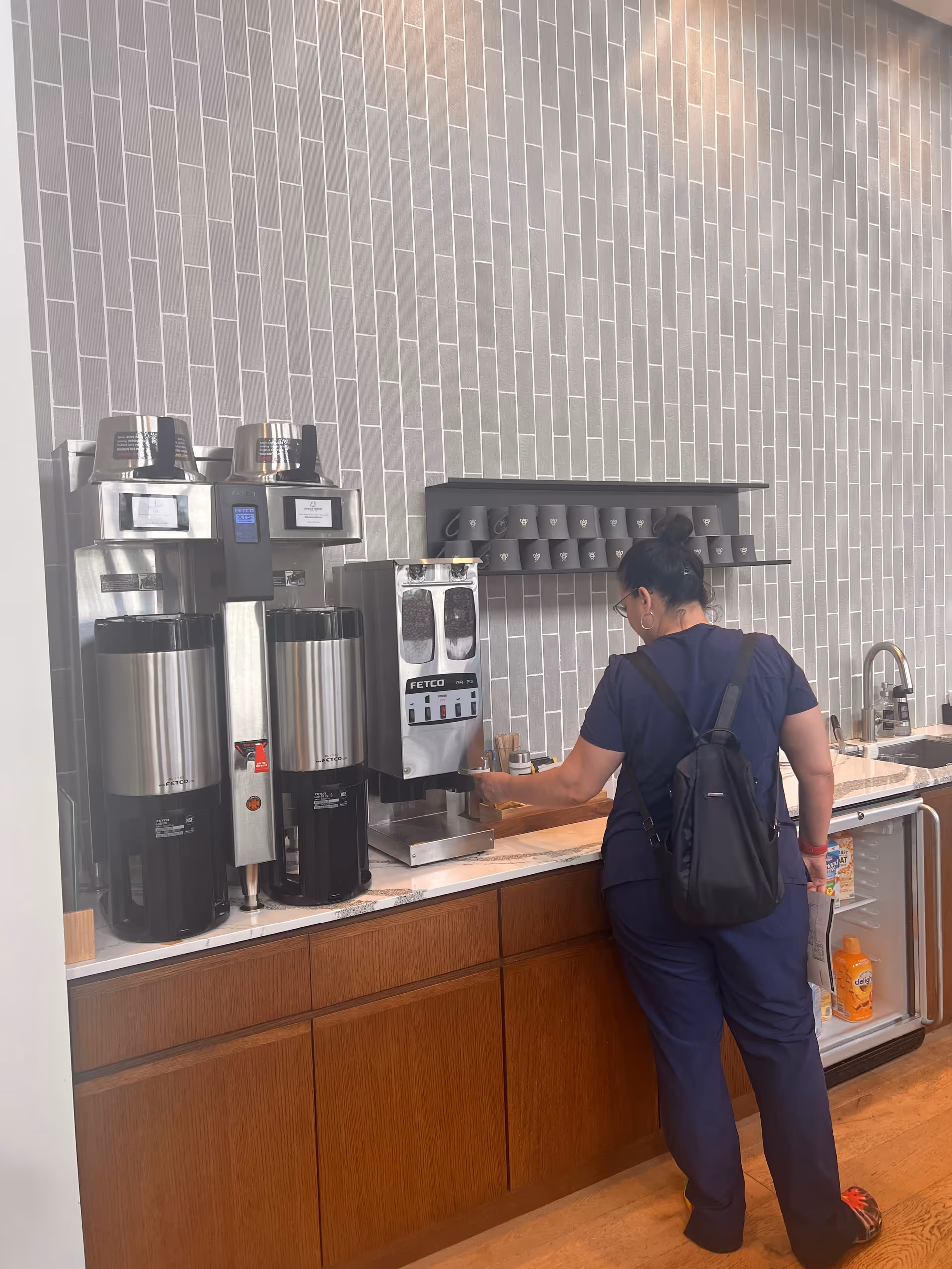 Staff member in scrubs prepares coffee at a modern kitchen counter.