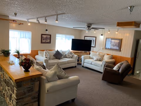 Cozy living room with couches, a TV, windows, and a stone bar counter.
