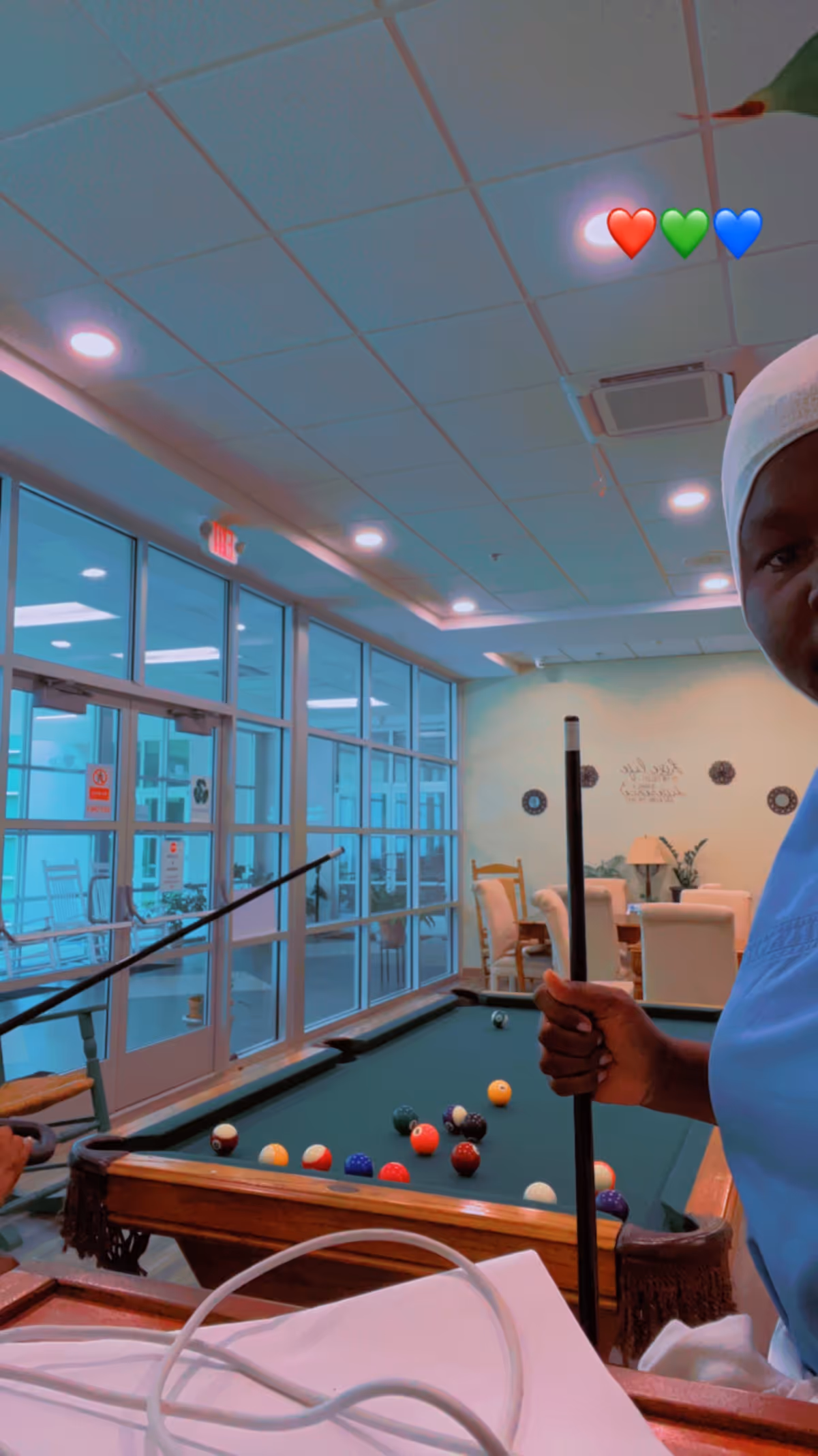 Indoor KalCare Health Care facility lounge with pool table, glass walls, and staff holding a cue.