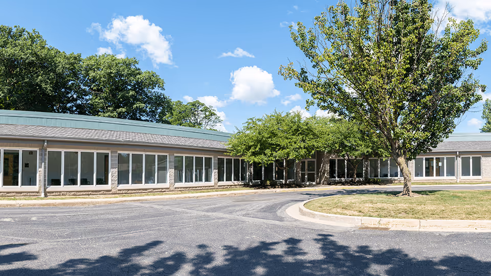 Single-story medical campus building with many glass doors, trees, and a curved driveway.