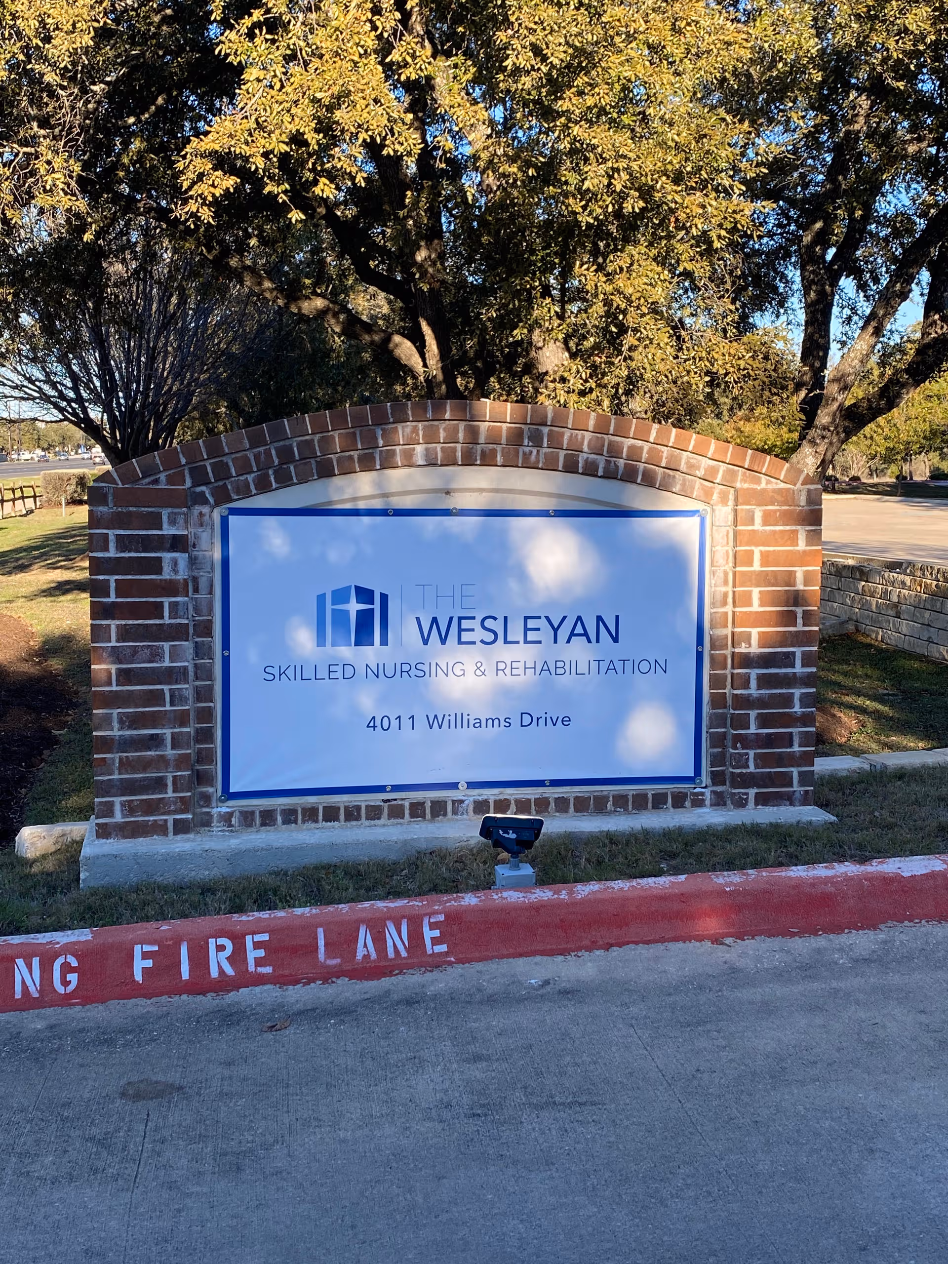 Brick sign for The Wesleyan Skilled Nursing and Rehabilitation logo in a landscaped outdoor area.