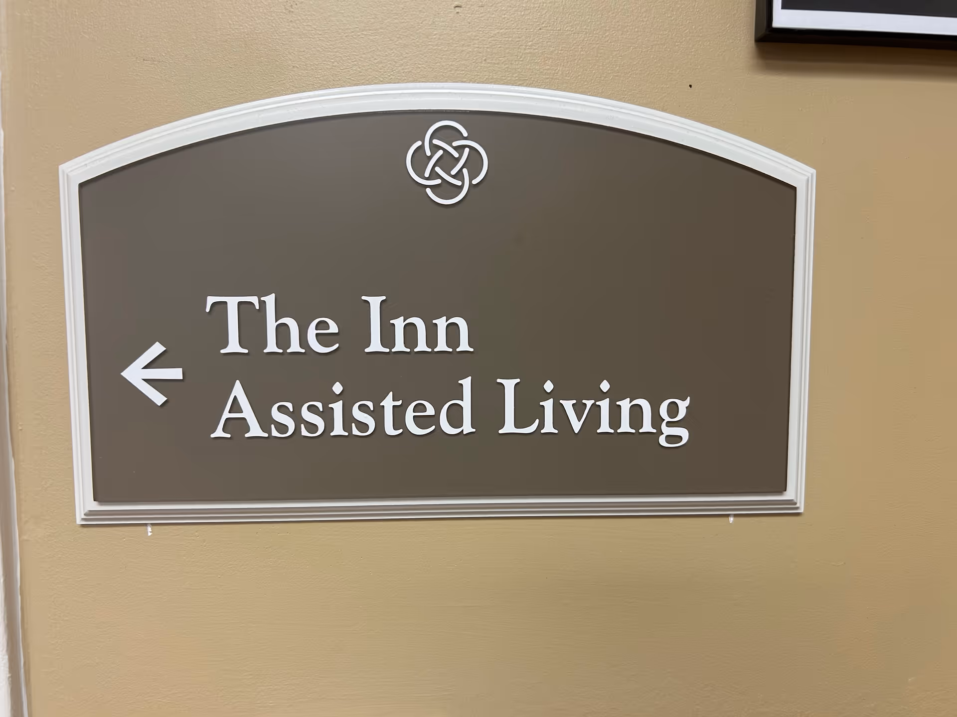 Brown sign on tan wall reading The Inn Assisted Living with left arrow