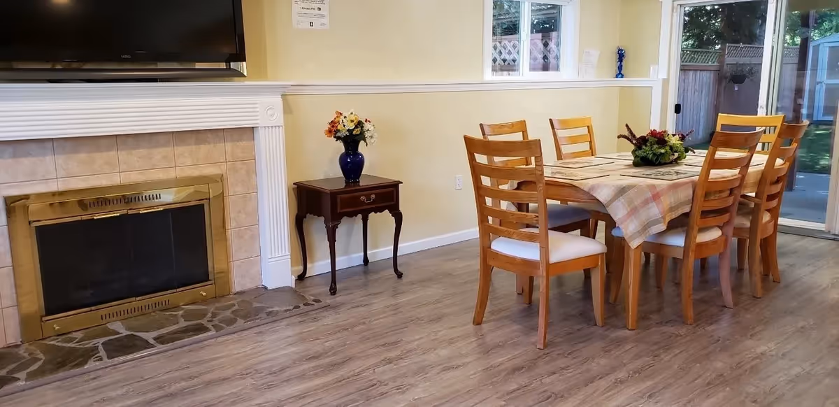 Dining area with a wooden table, six chairs, and a fireplace in a bright room.