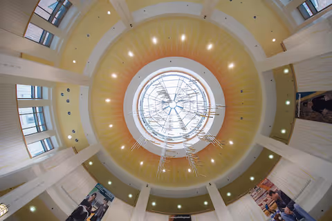 Circular atrium ceiling with skylight, warm yellow dome, and white surrounding columns.