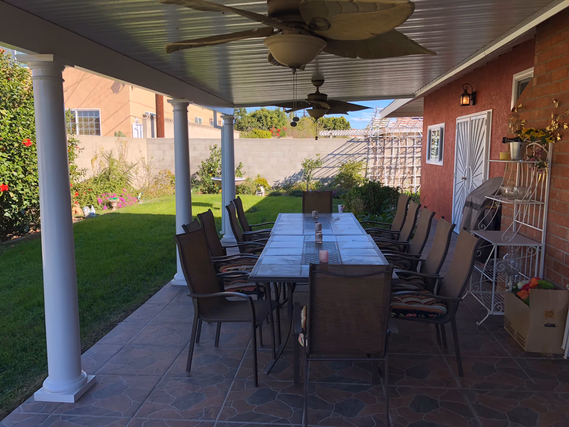 Long outdoor dining table with chairs under a covered patio in a backyard.
