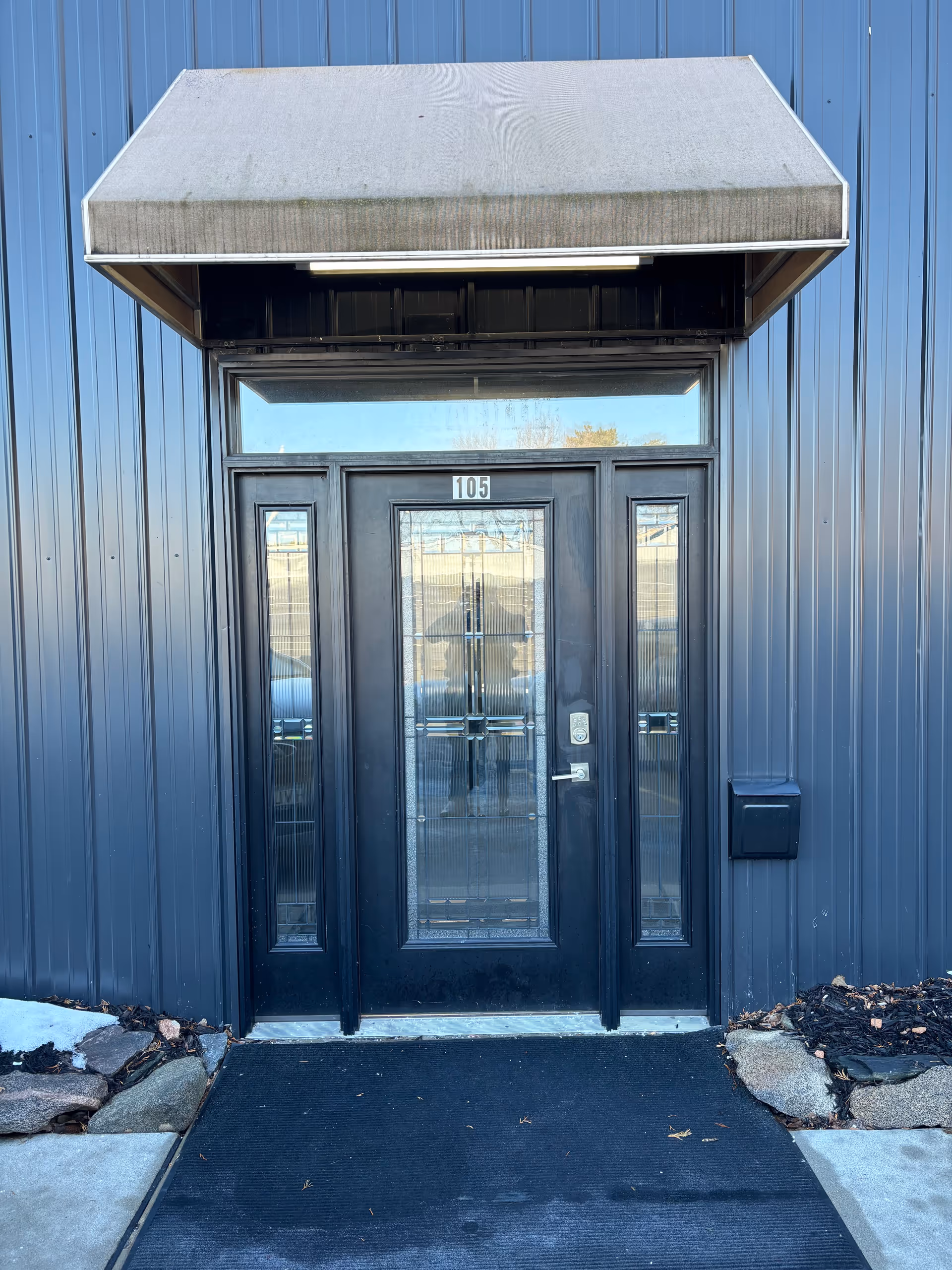 Blue metal exterior with a black glass door and a small canopy above.