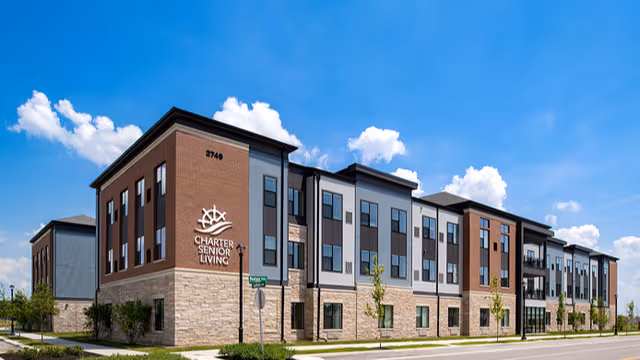 Facility exterior: Charter Senior Living building along street under blue sky.