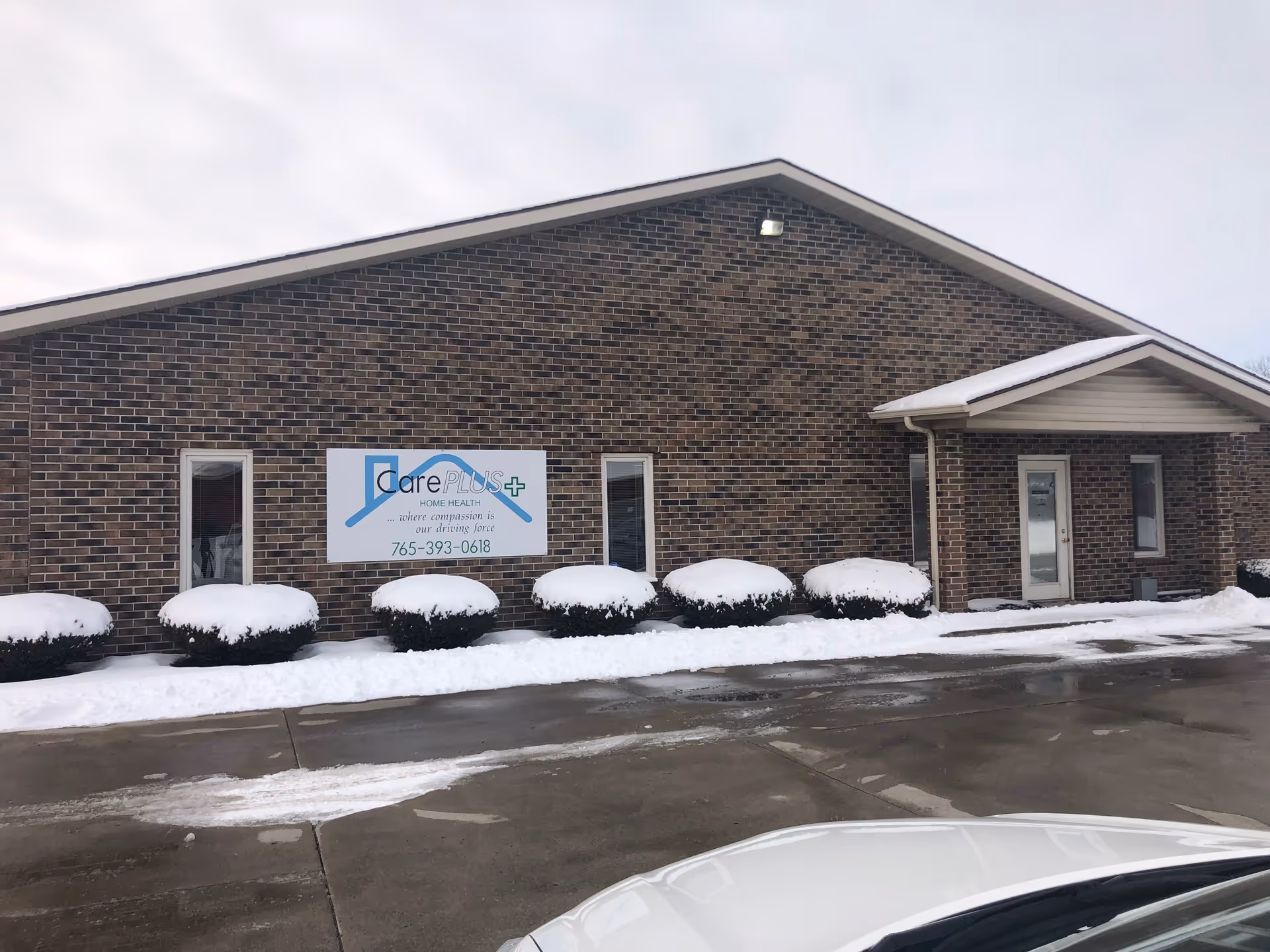 Brick facility exterior with Care Plus Home Health Care sign and snow-covered shrubs.