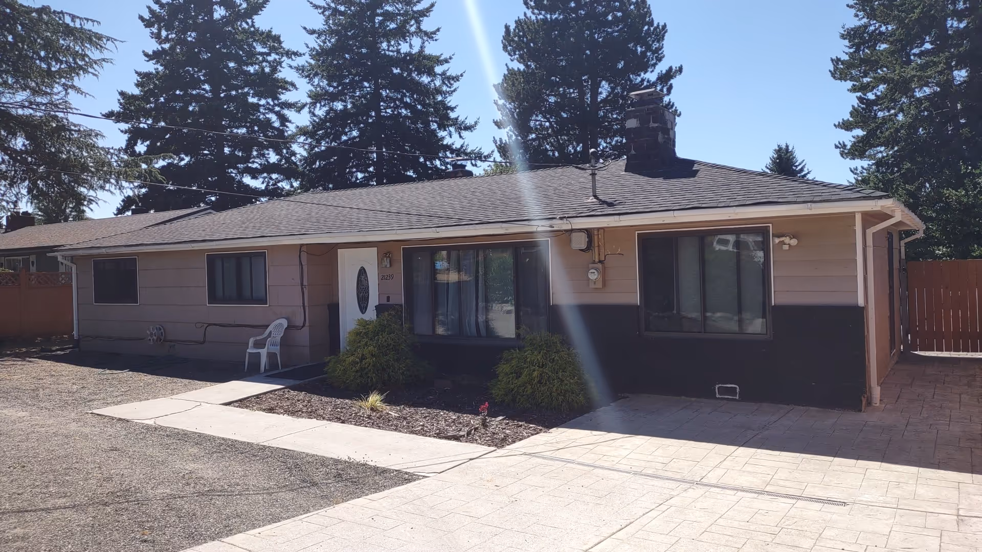 One-story beige house with front door, windows, and small shrubs.