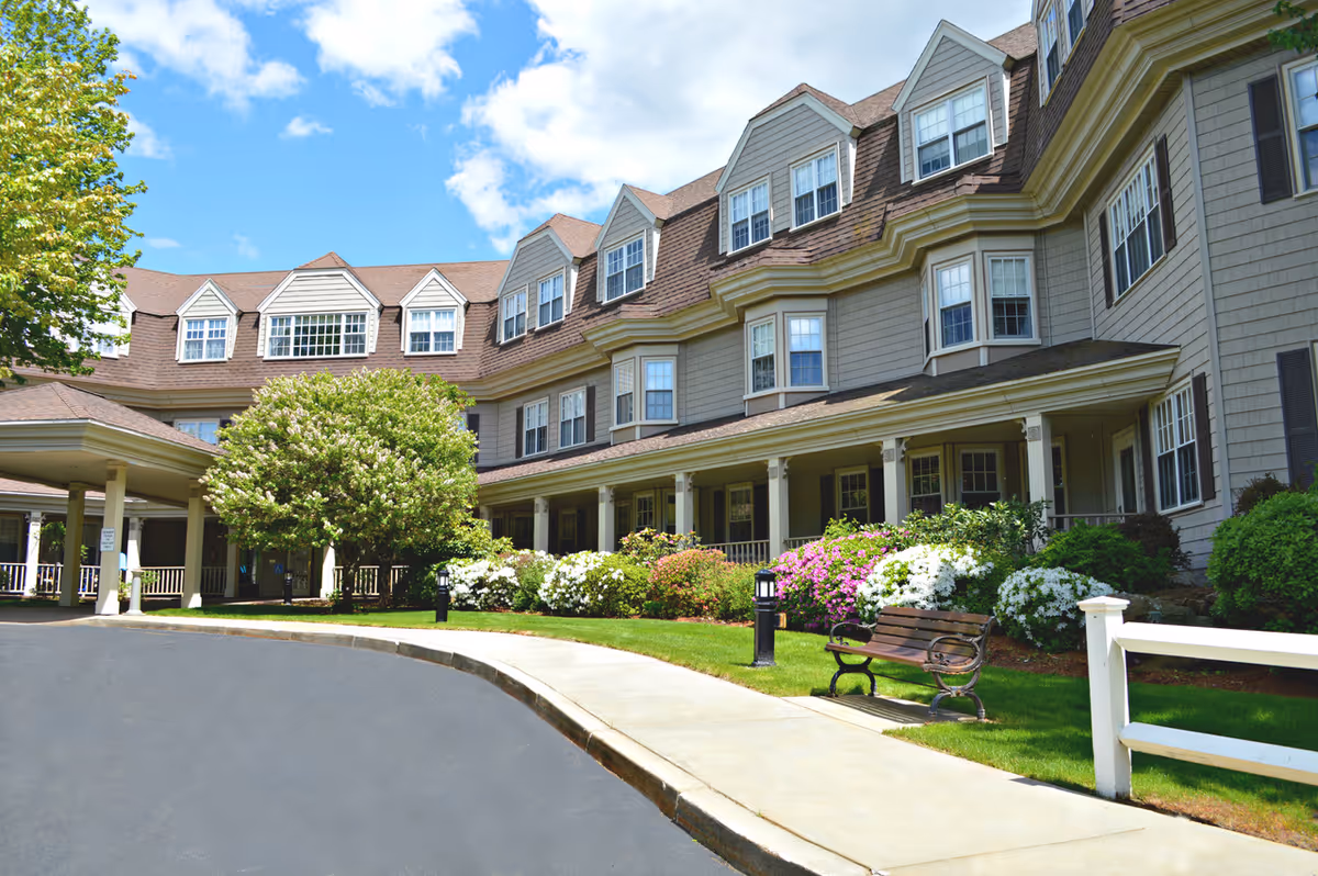 A large multi-story senior living facility exterior with a front porch and landscaping.