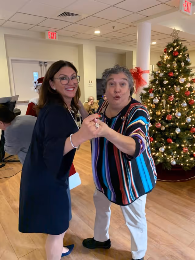 Two women smiling and dancing in a decorated common room next to a Christmas tree.