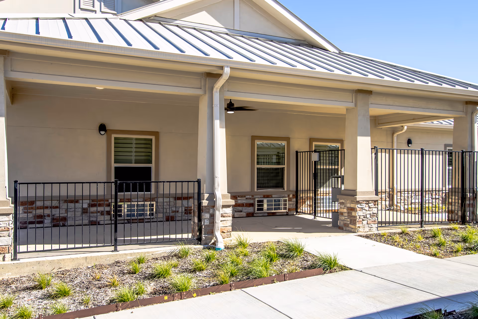 Exterior view of a senior living facility with a covered porch, railings, and gate.