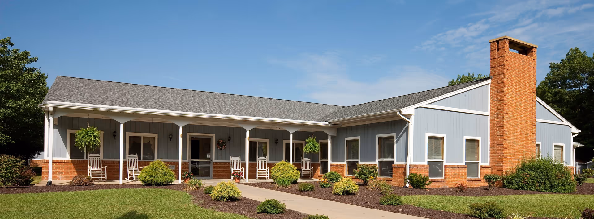Single-story light-blue senior living facility with a long front porch and rocking chairs.