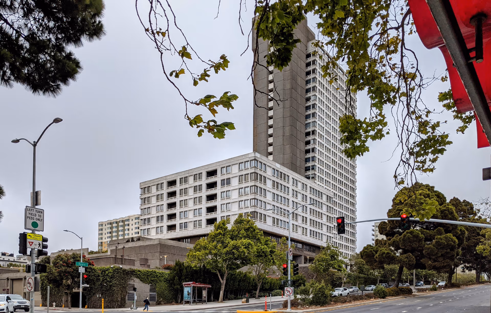 Tall modern senior living building beside a street with trees and traffic.