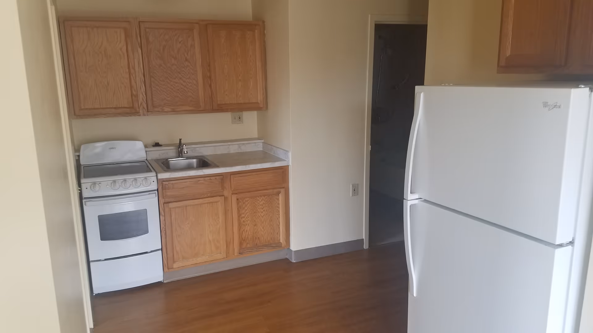 A small kitchenette with wooden cabinets, a sink, a compact stove, and a white refrigerator.
