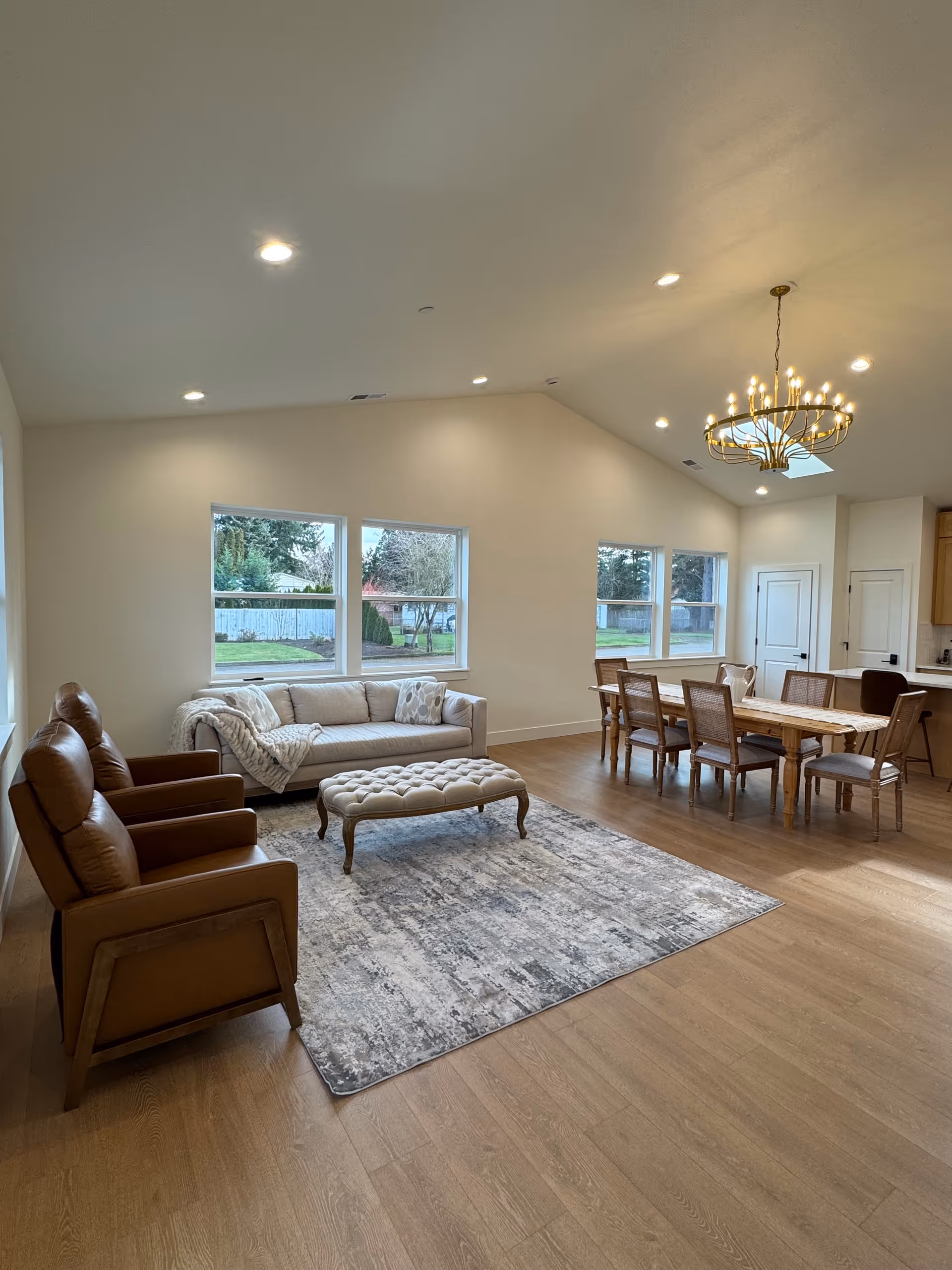 Bright open living area with sofa, chairs, ottoman, rug, and a dining table.